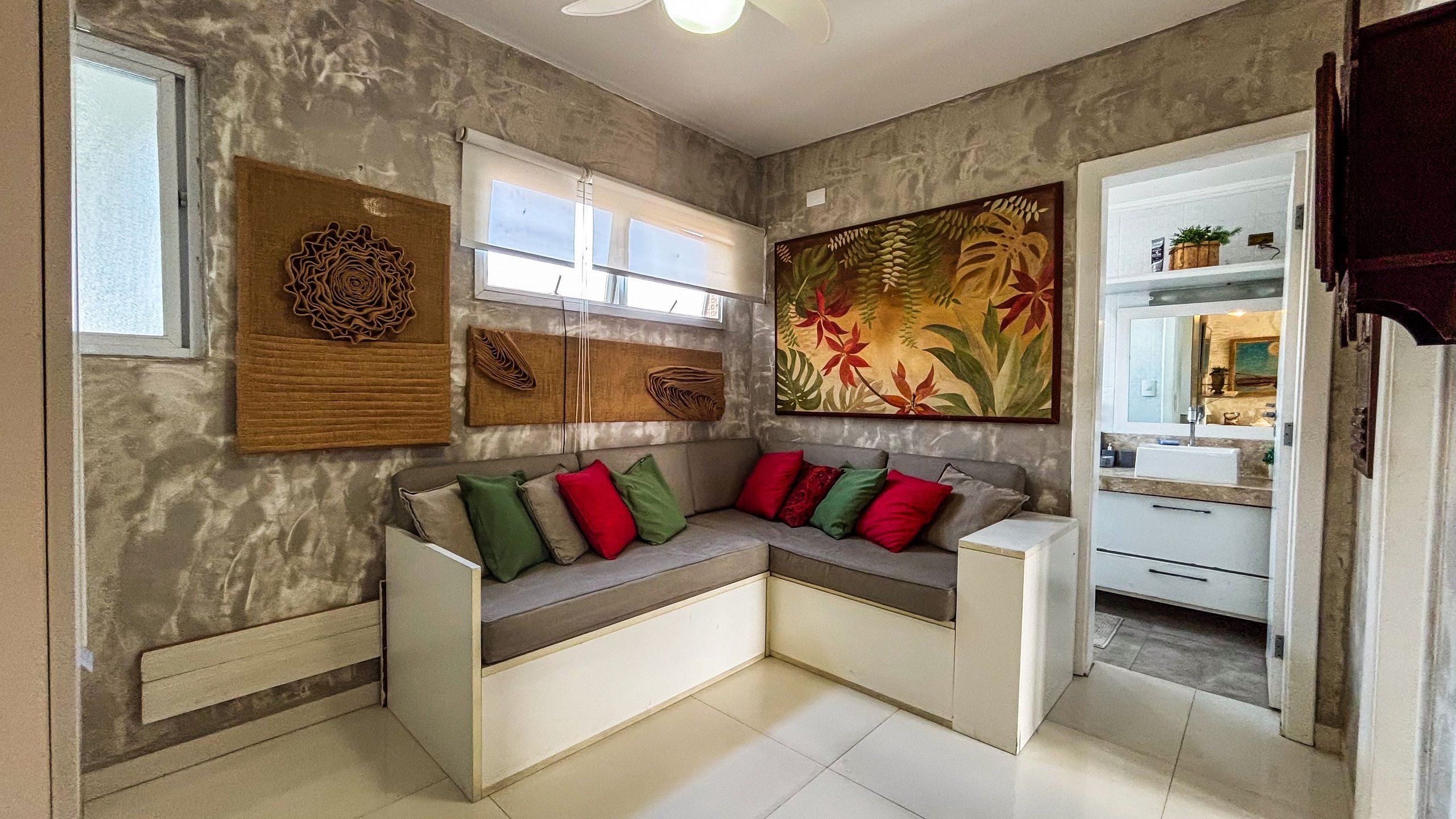 Una sala moderna con un sofá seccional, un cuadro floral grande y una cocina visible a través de una puerta abierta.