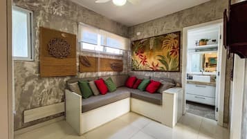 Una sala moderna con un sofá seccional, un cuadro floral grande y una cocina visible a través de una puerta abierta.