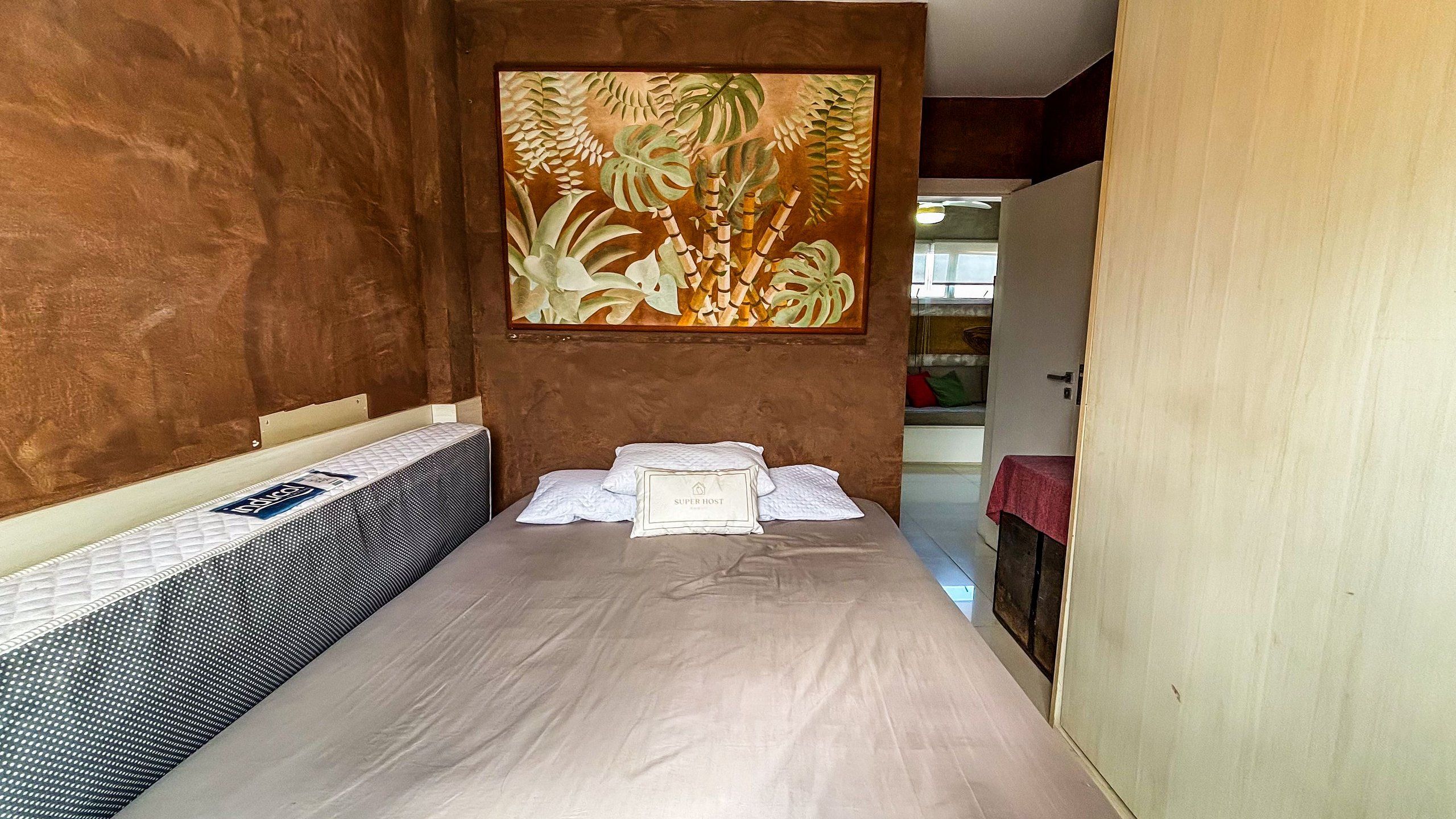 Una habitación con una cama, una obra de arte colgada en la pared y una puerta que da a otra estancia.