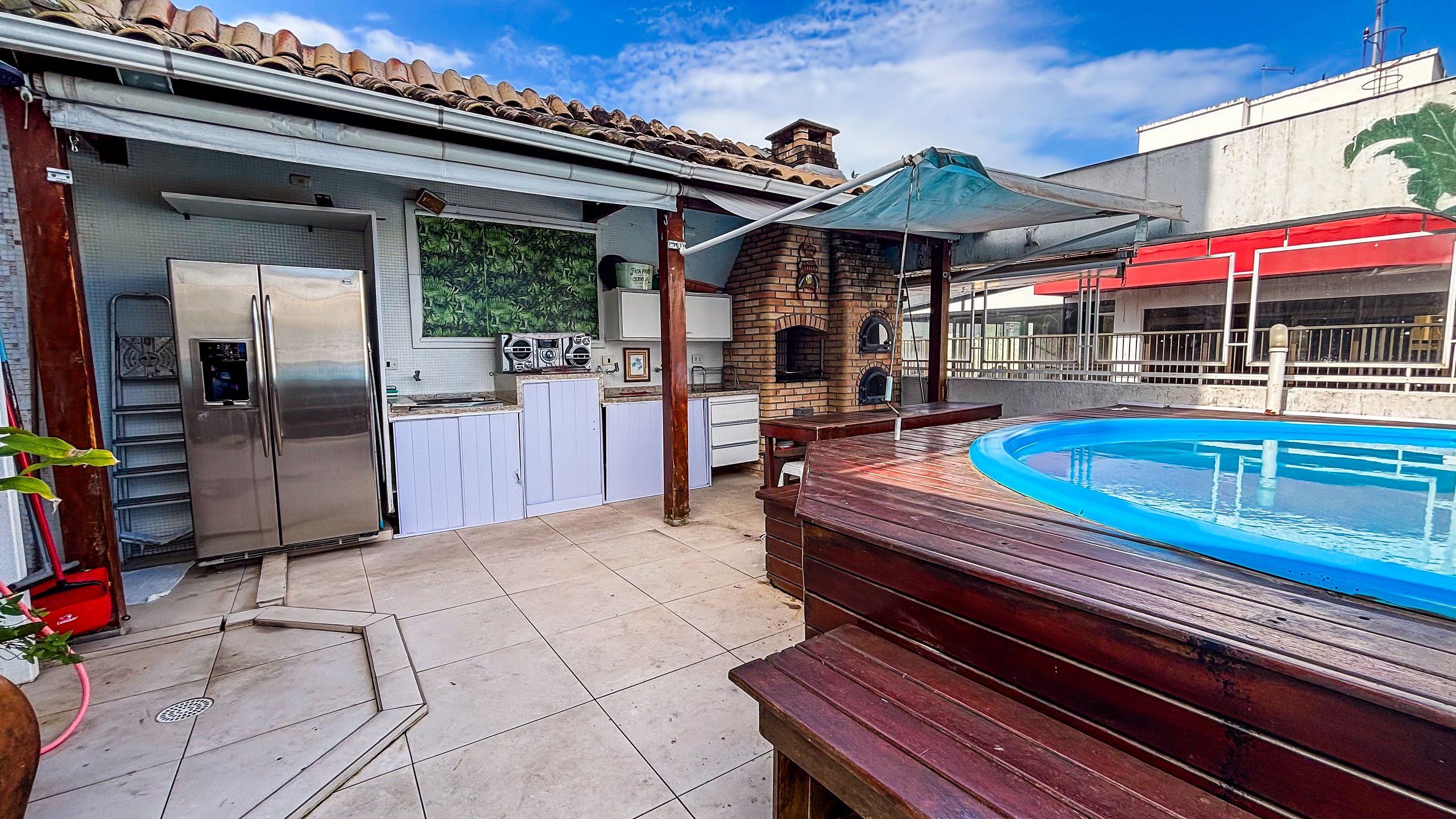 Patio trasero con piscina, zona de barbacoa y cocina con refrigerador.