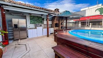 Patio trasero con piscina, zona de barbacoa y cocina con refrigerador.
