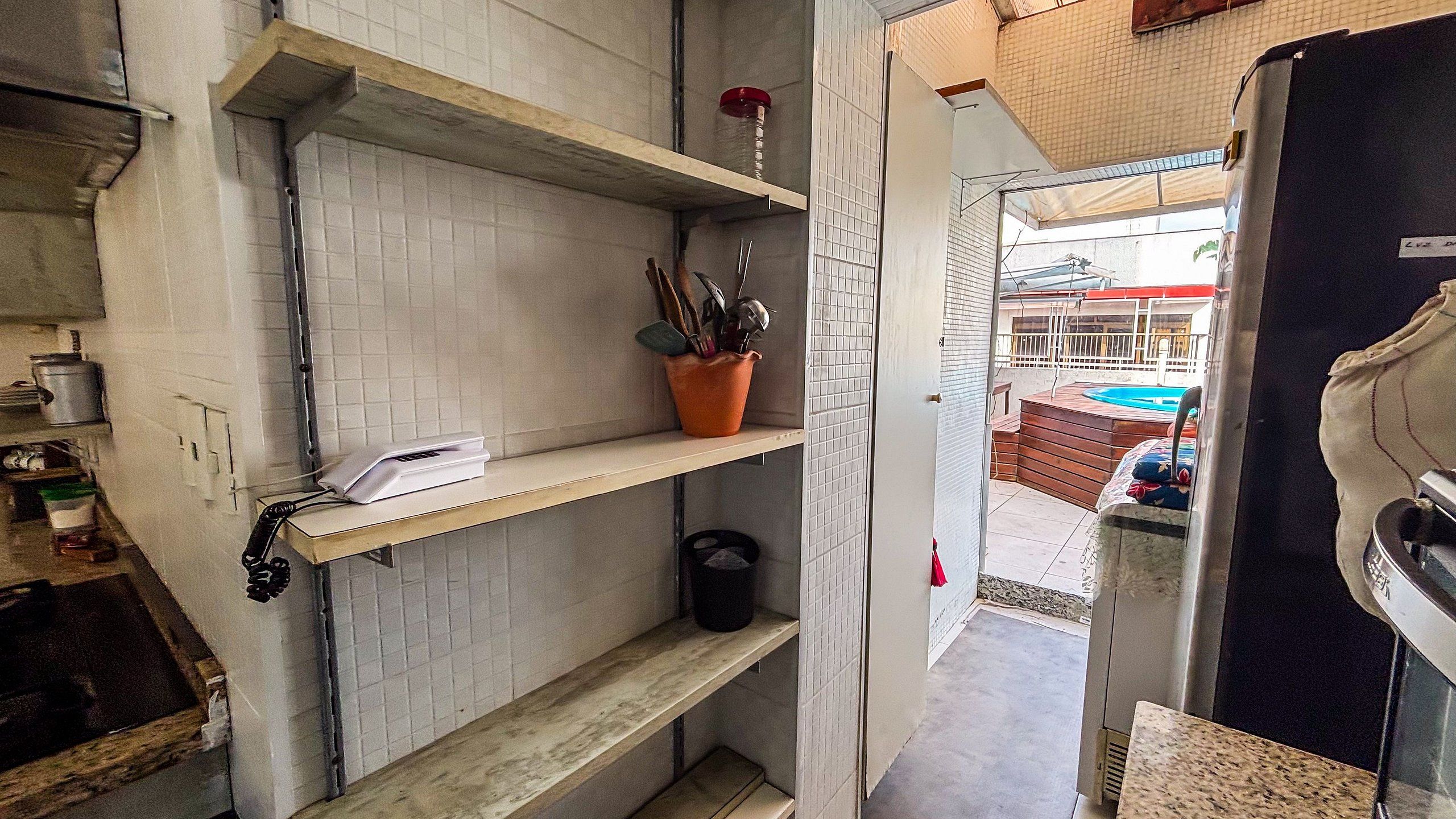 Una cocina con paredes de azulejos blancos, estantes de madera y una planta en maceta.