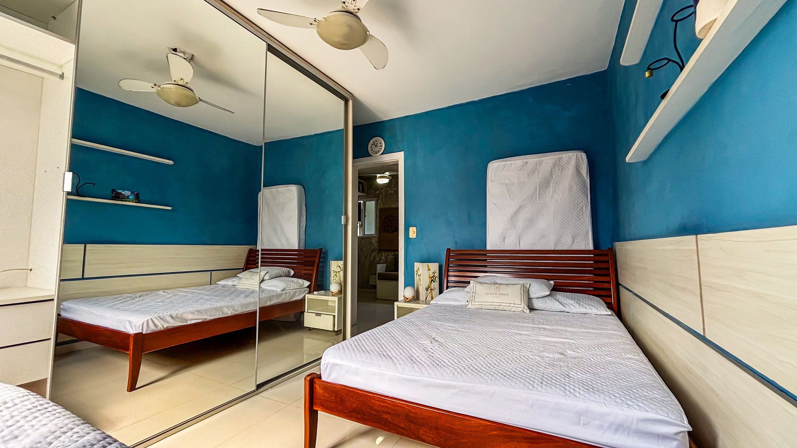 Un dormitorio con dos camas, un espejo, ventiladores de techo y un reloj en la pared.