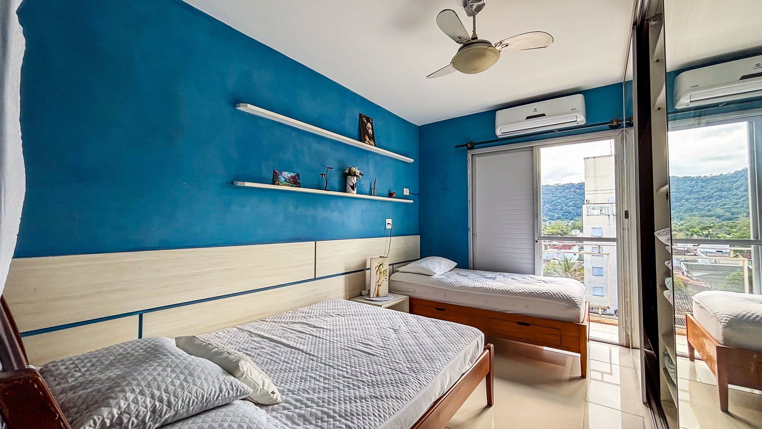 Un dormitorio con dos camas, ventilador de techo, ventana con vistas y unidad de aire acondicionado.