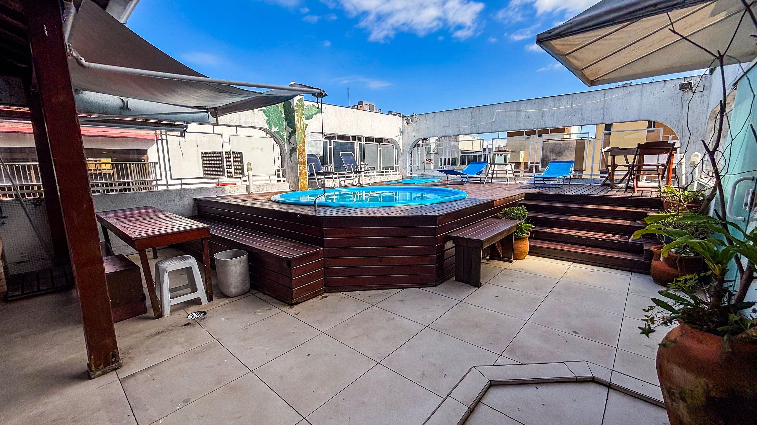 Um pátio externo com banheira de hidromassagem, assentos de madeira e piscina.