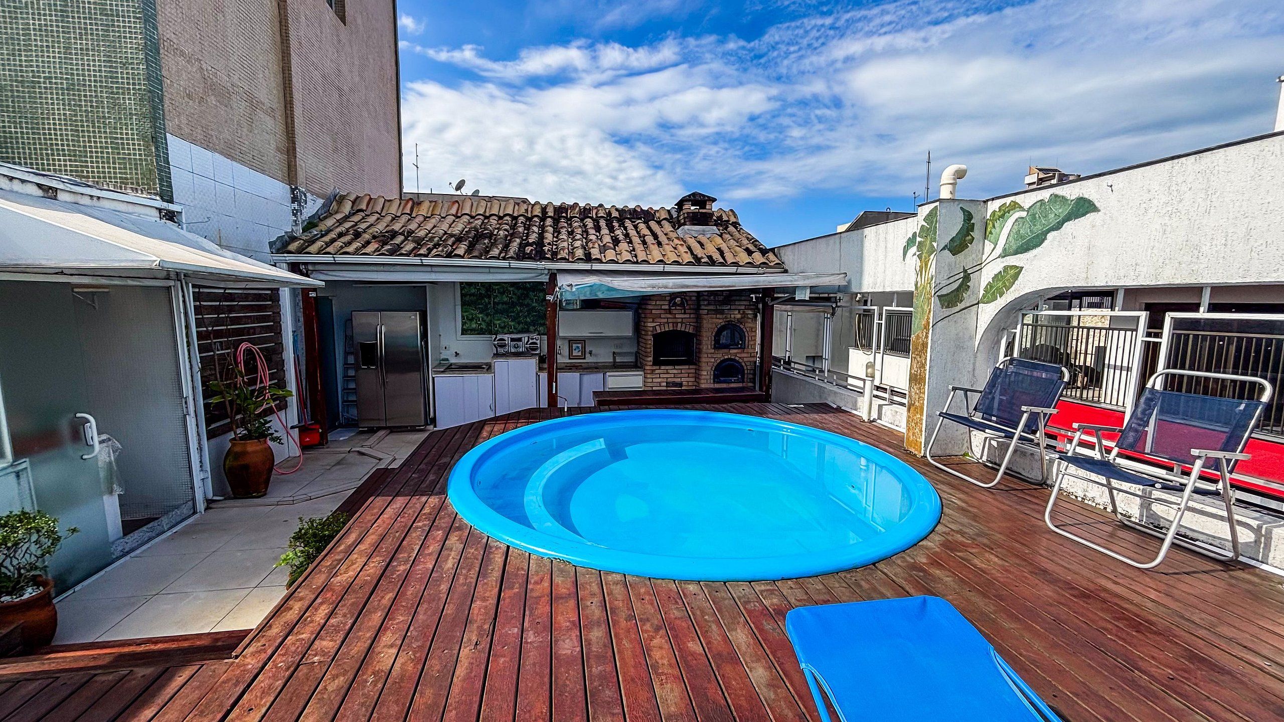 Un patio trasero con piscina, terraza de madera, cocina al aire libre y un área de patio cubierta.