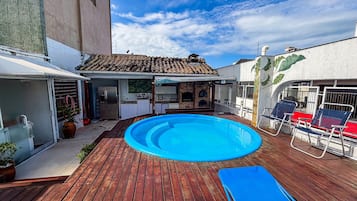 Un patio trasero con piscina, terraza de madera, cocina al aire libre y un área de patio cubierta.
