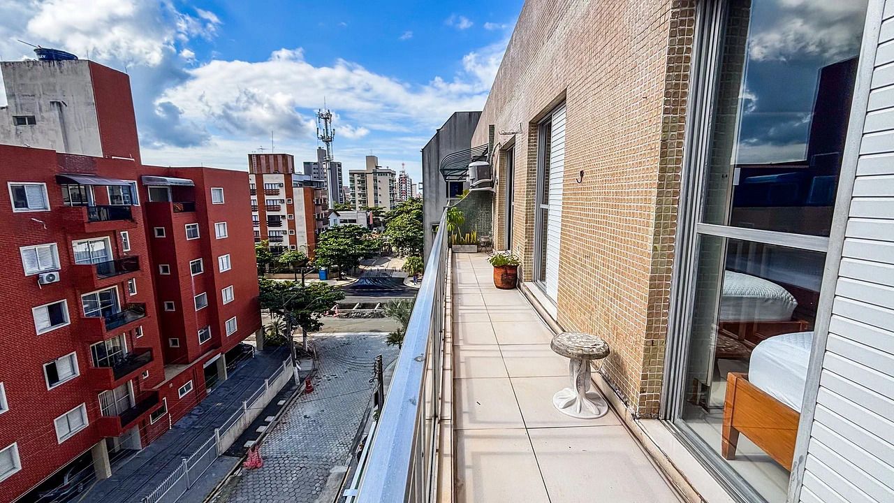 Un balcón estrecho con vistas a un paisaje urbano, una mesa pequeña y una planta en maceta.