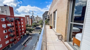 A narrow balcony with a view of a cityscape, a small table, and a potted plant. - SHB Cobertura e Piscina Privativa  (GUARUJÁ)