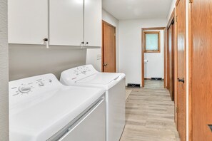 Un área de lavandería con dos lavadoras de carga frontal, una puerta de madera y un pasillo que conduce a una ventana.
