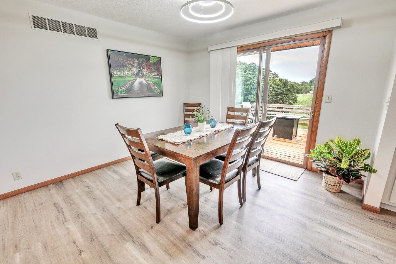 Un coin repas avec une table et des chaises en bois, un tableau accroché au mur et une vue à travers une porte vitrée.