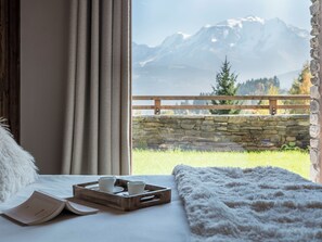 Ein Zimmer mit einem Bett, einem Vorhangfenster, einem Tablett mit Tassen und Blick auf Berge.