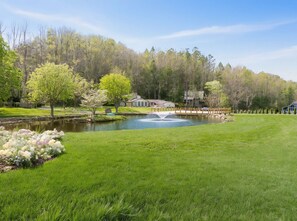A serene landscape with a pond, lush green lawn, and a wooden bridge. - Beautiful Waterfront Estate! Close to Gatlinburg!  4 Suites, Hot Tub & Game Room (Pittman center)