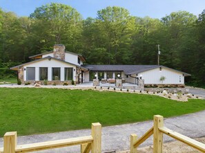 Une maison moderne à deux étages, dotée d’une cheminée en pierre, de grandes fenêtres et d’une pelouse bien entretenue.
