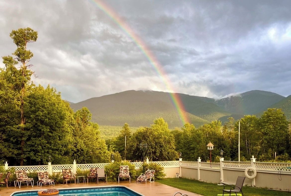 A swimming pool with lounge chairs, a white fence, and a mountain backdrop.