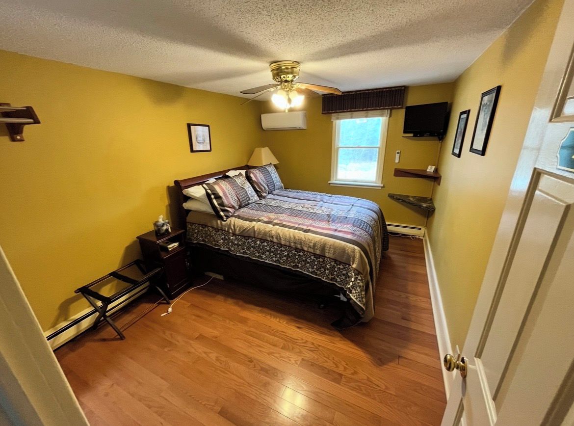 A bedroom with a bed, a ceiling fan, a window, and a door.