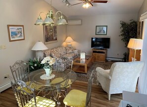 A living room with a sofa, a coffee table, a TV, a lamp, and a ceiling fan. - Bowman inn Spacious 12-bedroom estate in beautiful Randolph with AC/pool/hottub (Randolph)