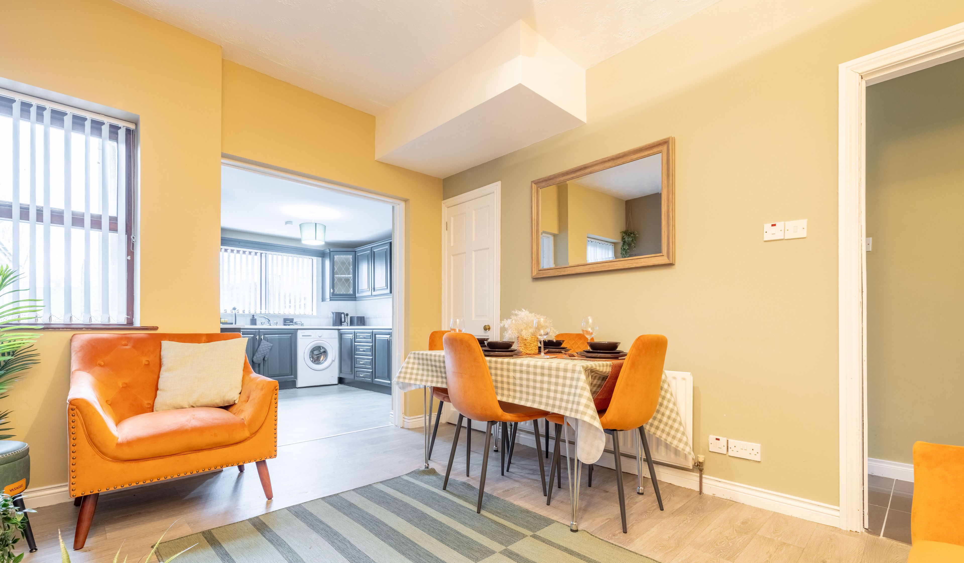 Un coin repas avec une table dressée pour quatre personnes, un canapé et une cuisine en arrière-plan.