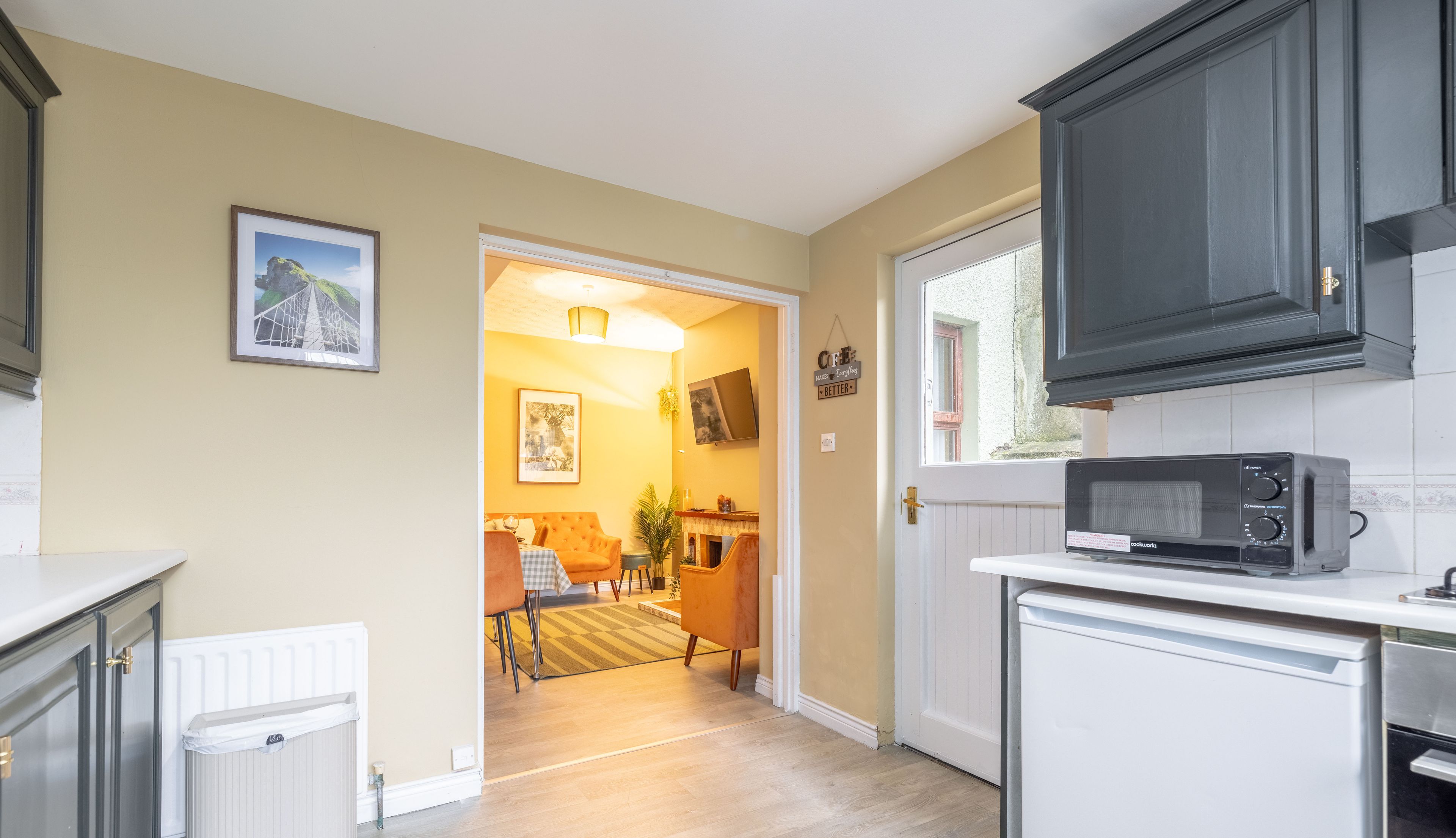 A kitchen with a microwave, a white cabinet, and a door leading to a dining area with a table and chairs.