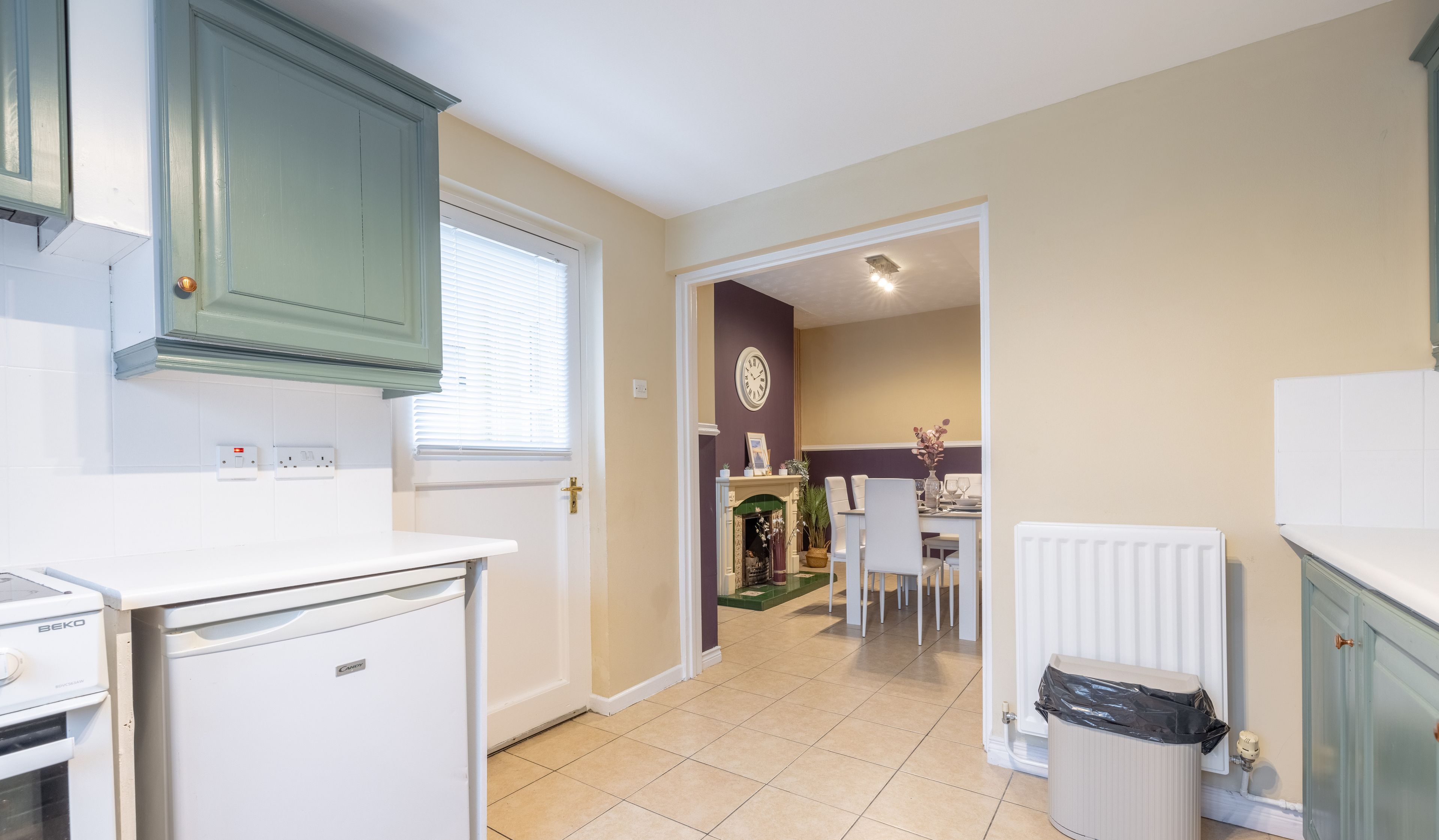 A compact kitchen with a built-in oven, a small refrigerator, and a window with blinds.
