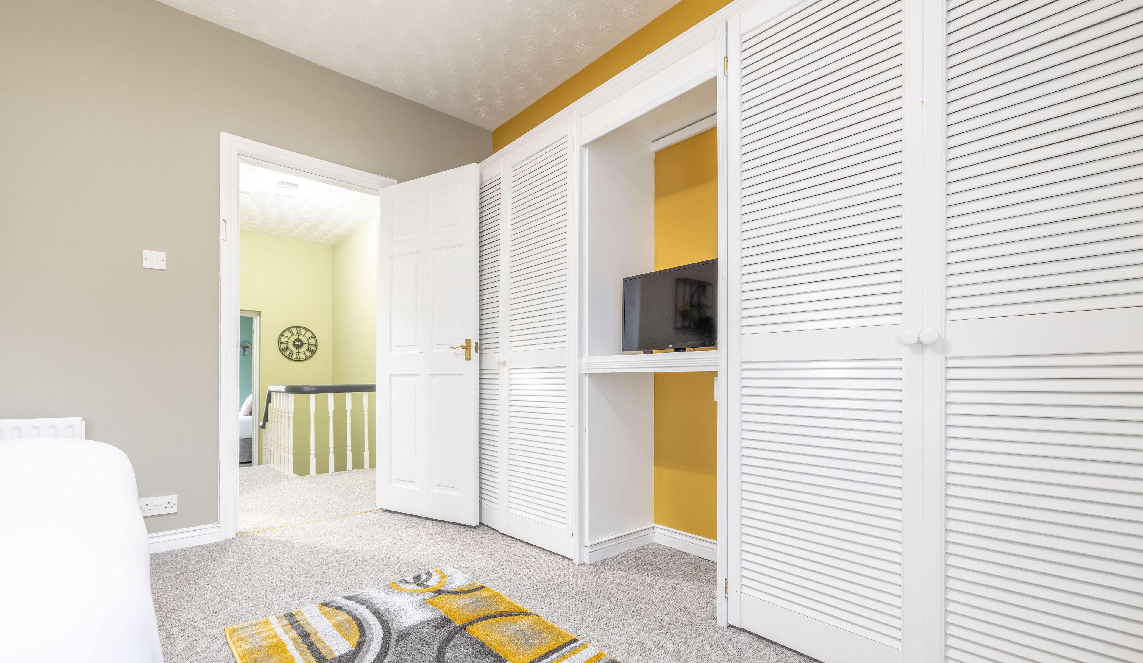 A room with a white door, a yellow wall, and a television on a shelf.
