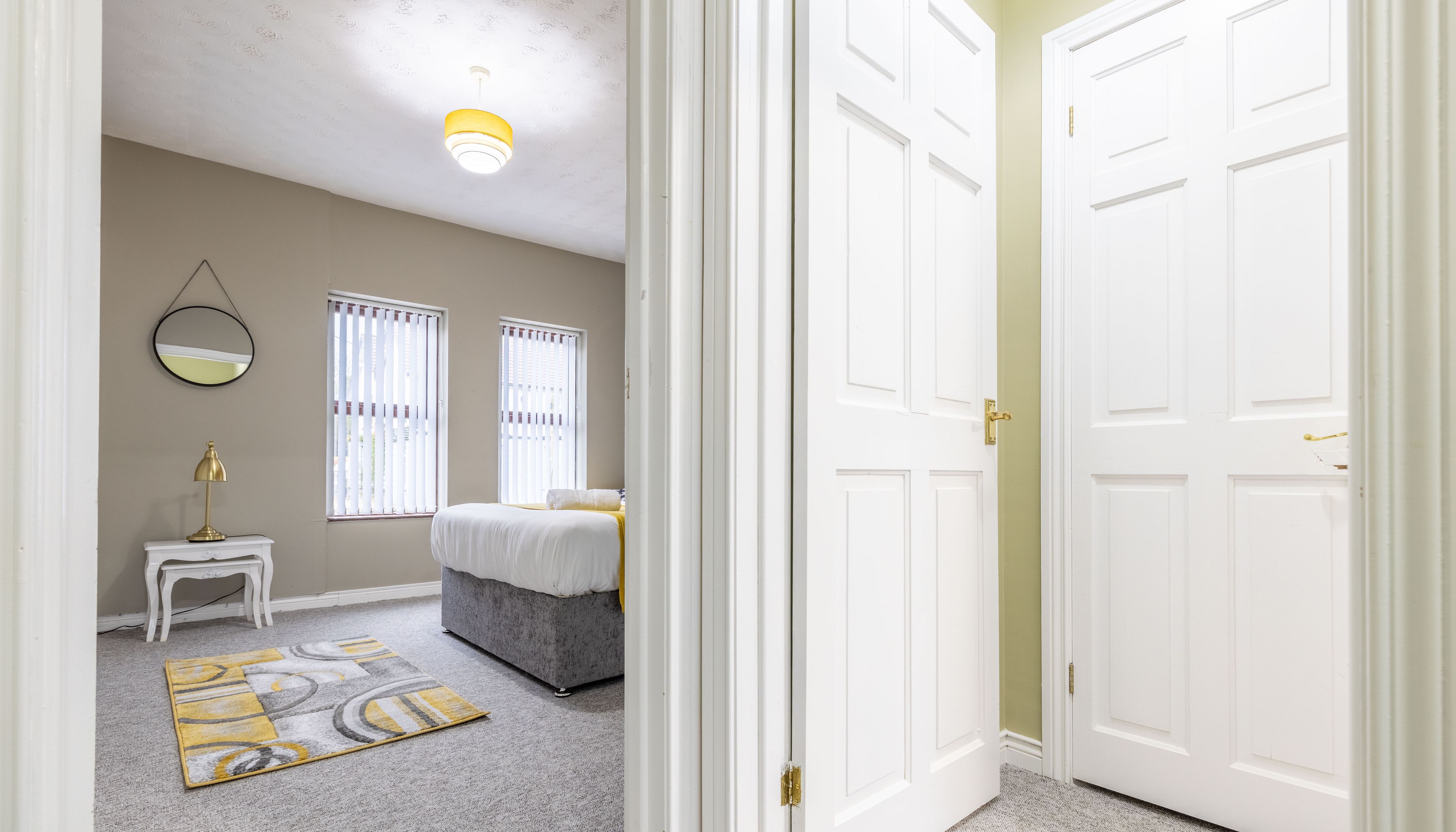 A bedroom with a bed, bedside table, lamp, and a mirror on the wall.