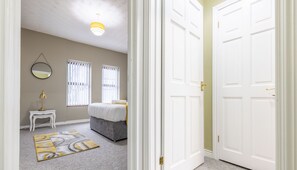 A bedroom with a bed, bedside table, lamp, and a mirror on the wall. - Coastal Cottages (Ballycastle)