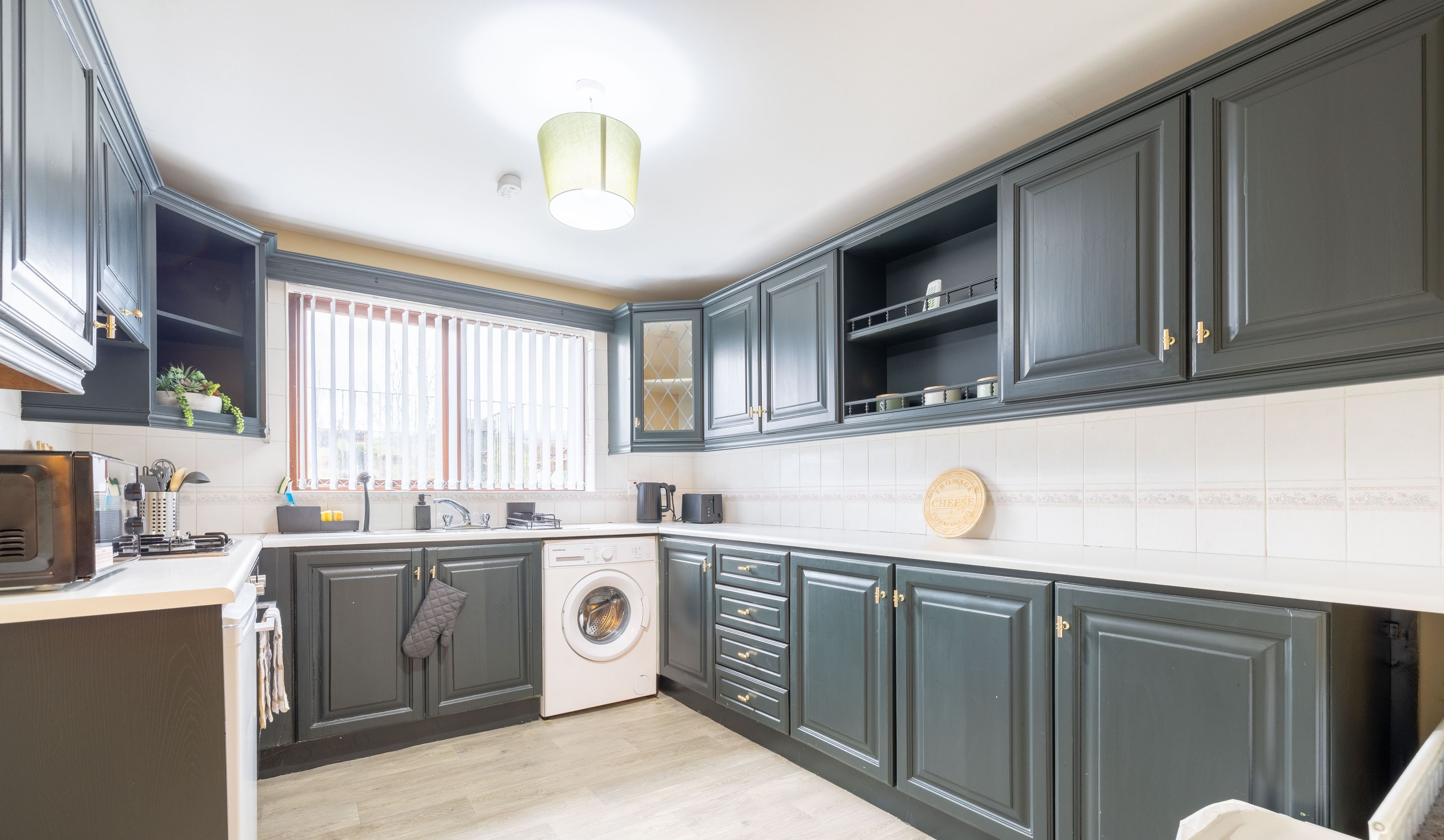 A modern kitchen with dark cabinetry, a built-in washing machine, and a window with blinds.