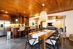 A modern kitchen with wooden cabinets, a stainless steel refrigerator, and a dining area with a long wooden table and chairs. - Playa Langosta Penthouse with Pool and private jacuzzi (Playa Langosta)