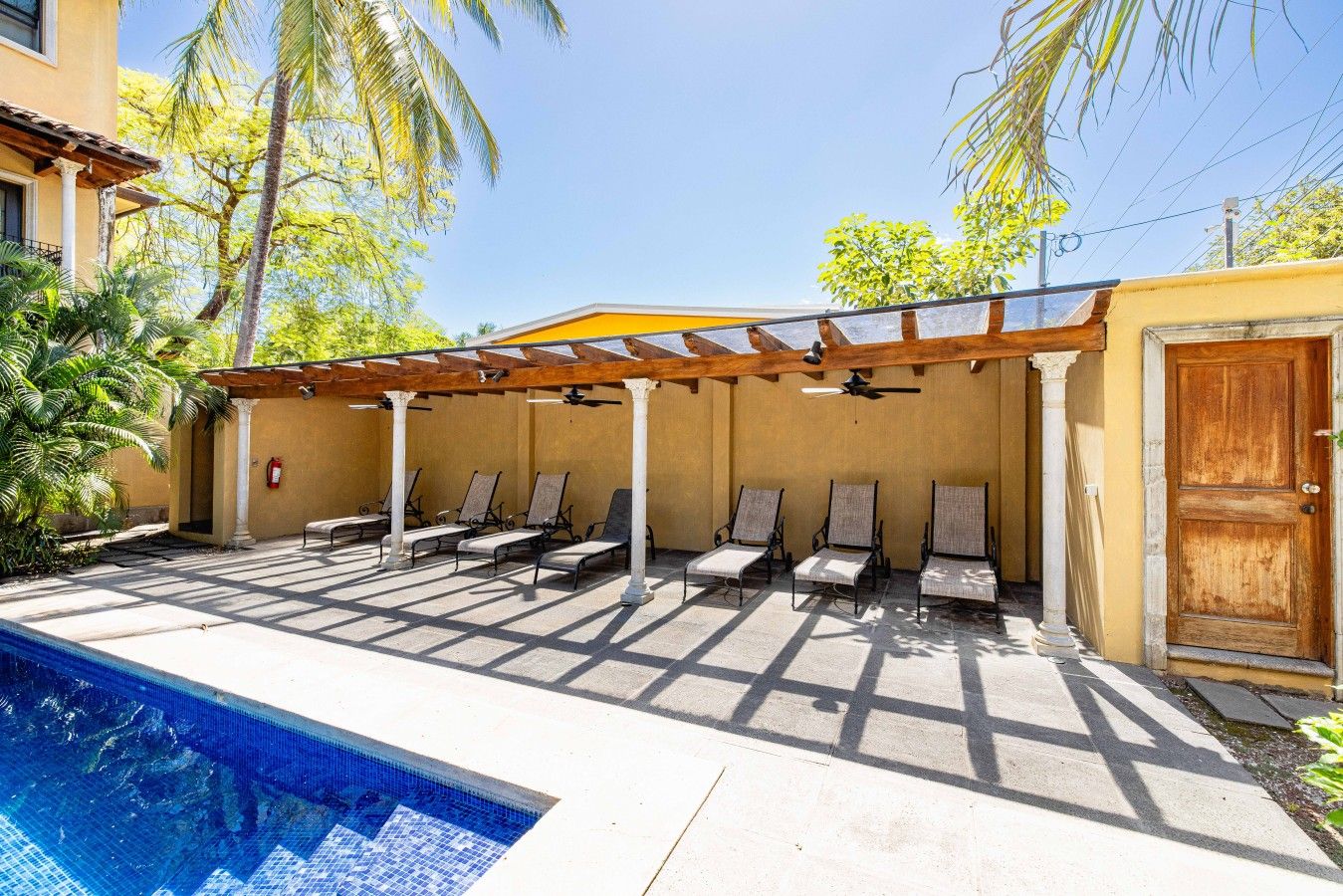 Un espace aménagé au bord de la piscine, comprenant une pergola, des chaises longues et une porte.