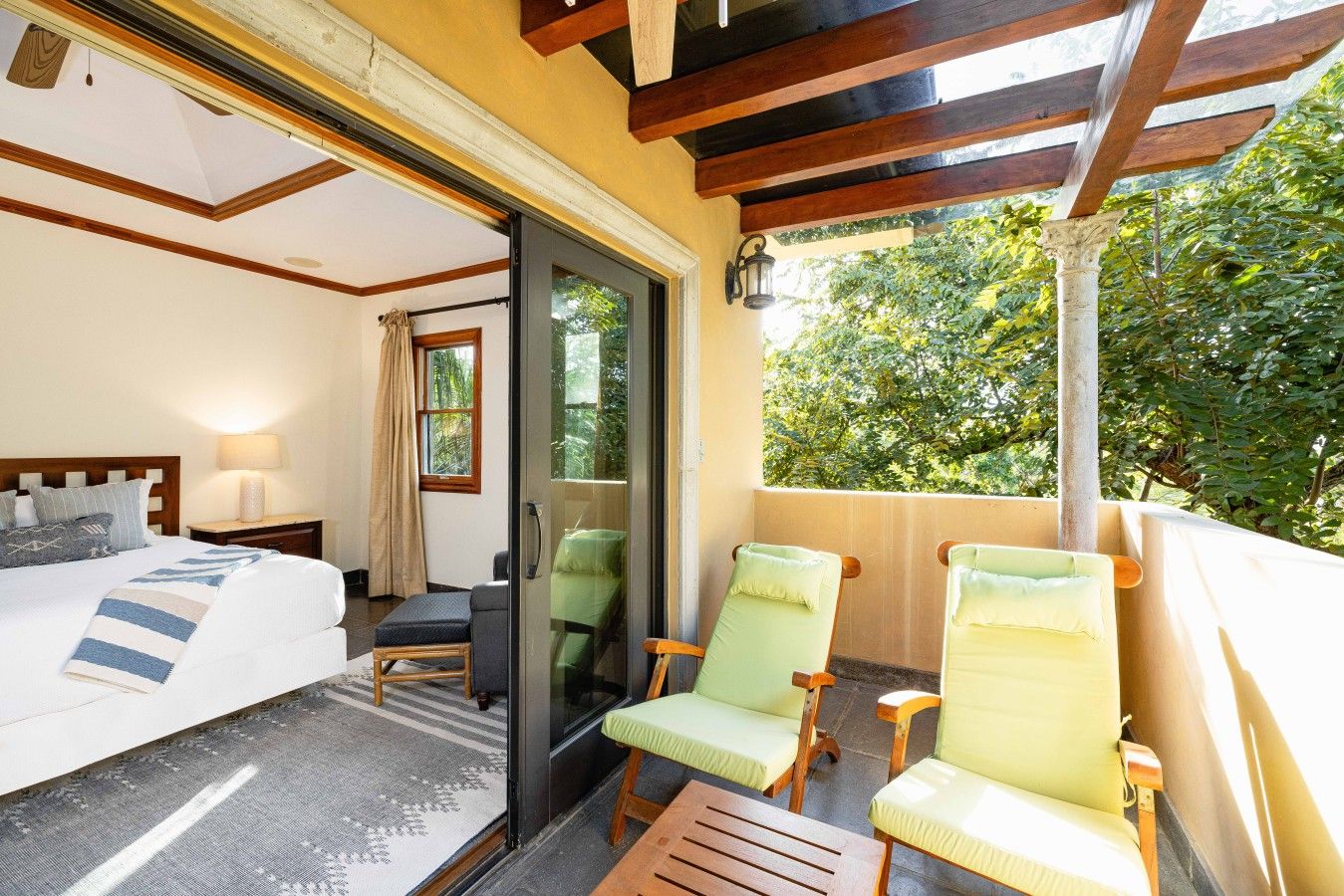 A hotel room with a bed, a desk, two chairs, and a balcony with a view of trees.