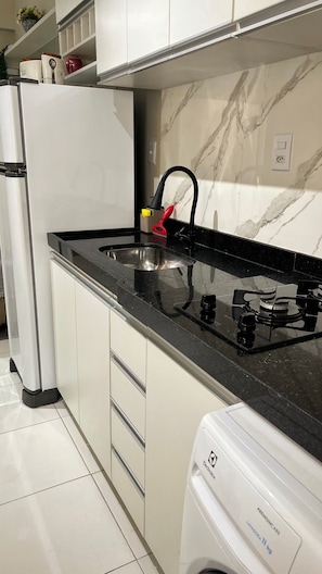 A kitchen with a black countertop, white cabinets, a stainless steel sink, and a white washing machine. - 105 · 105 AP 2 Bedrooms Practical and Functional (Belém)