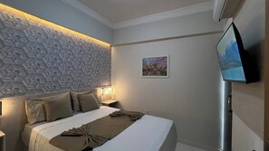 Une chambre d’hôtel avec un lit, un téléviseur fixé au mur et un mur orné d’un motif géométrique.