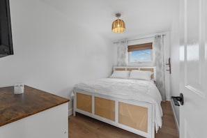 A bedroom with a bed, a bedside table, a window with curtains, and a hanging light fixture.