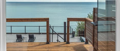 A view from a balcony with a wooden deck, overlooking a body of water and a clear sky.