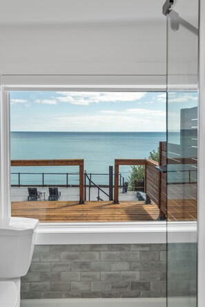 Blick vom Balkon mit Holzterrasse auf ein Gewässer und einen klaren Himmel.
