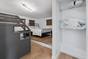 Une chambre avec un lit superposé, une table de chevet, une armoire avec des étagères et une fenêtre avec des stores.