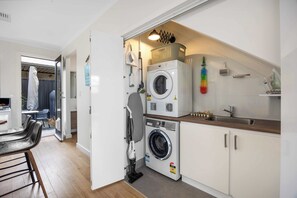 A compact laundry room with a washing machine, dryer, and ironing station. - The Onka Contemporary Escape by the Coast (Port Noarlunga)
