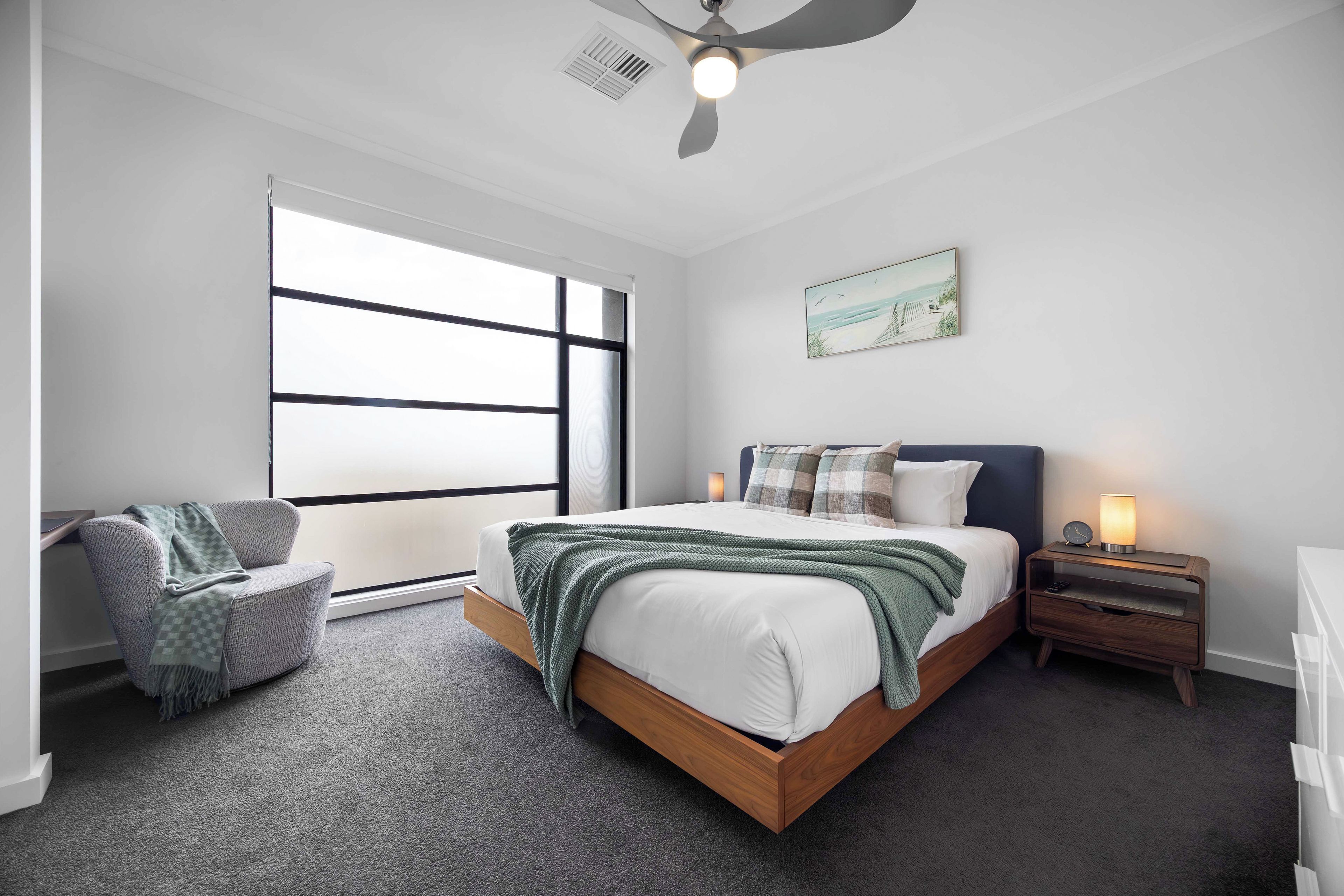 A bedroom with a bed, a chair, a nightstand, a lamp, and a ceiling fan.