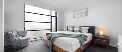 A bedroom with a bed, a chair, a nightstand, a lamp, and a ceiling fan.