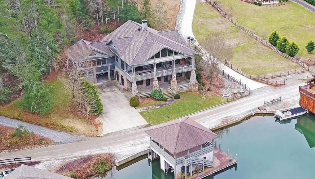 Una casa grande de dos pisos con un porche cubierto, un muelle y un bote pequeño.