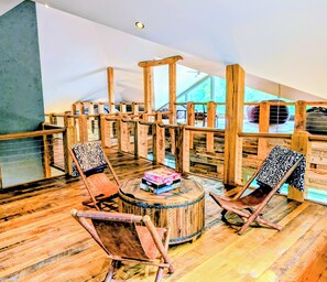 Un espace de détente au sol en bois, comprenant deux chaises en bois et une table ronde en bois, offrant une vue à travers une balustrade en bois.