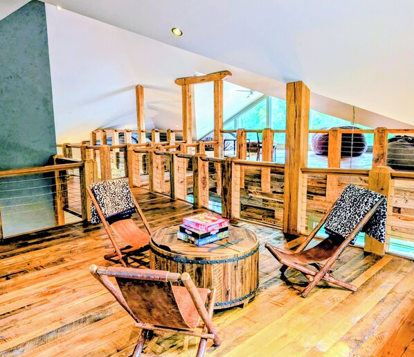 A wooden-floored lounge area with two wooden chairs and a round wooden table, featuring a view through a wooden railing.