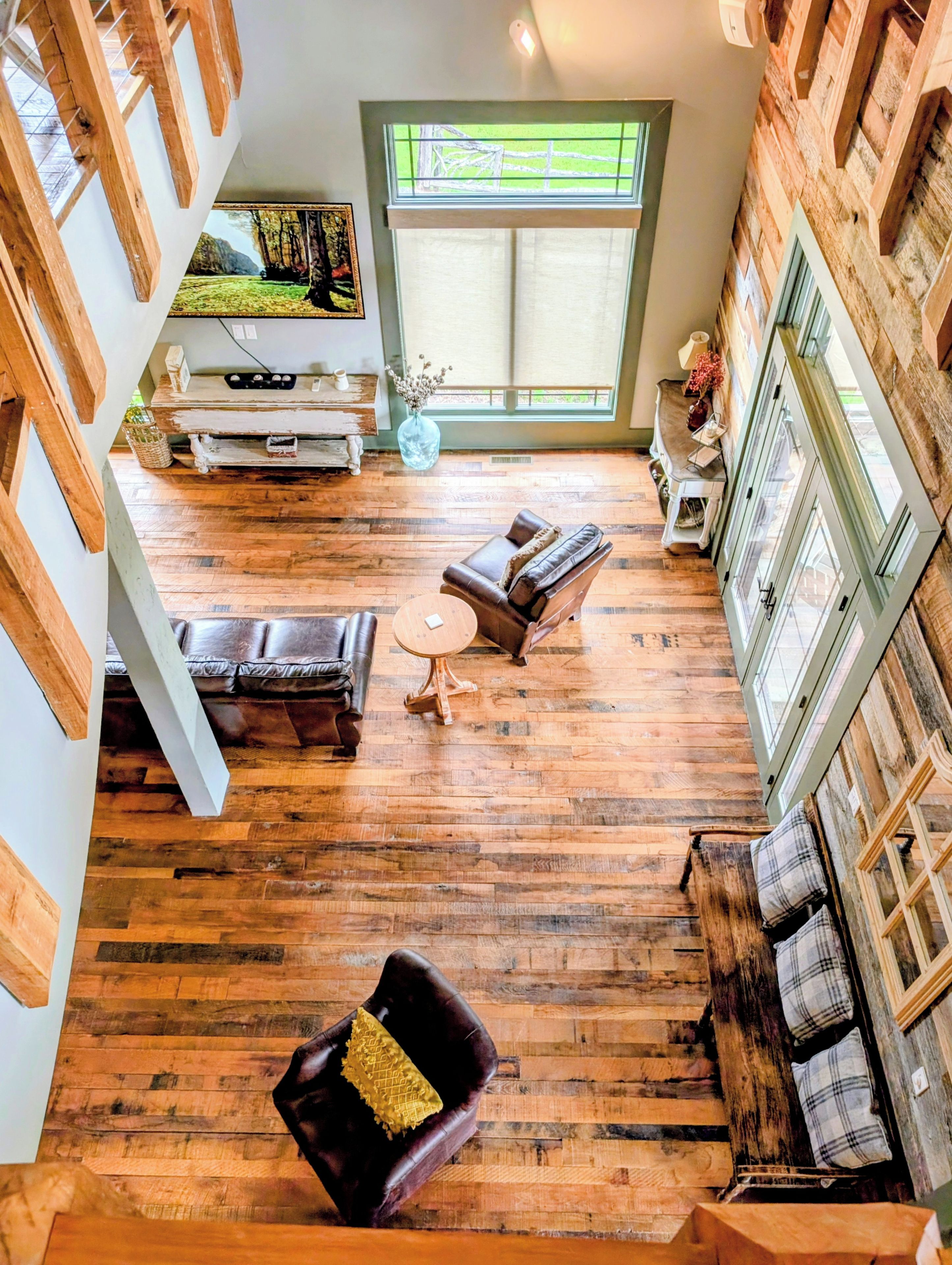 A spacious room with a wooden floor, a leather sofa, a round coffee table, and a large window with a view of greenery.