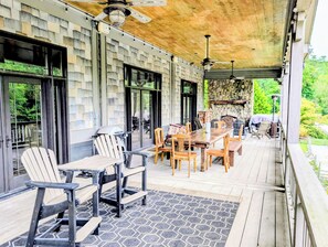 Een overdekt terras buiten met een houten terras, een stenen muur en een stenen open haard.