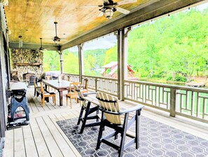 Un espace extérieur abrité, doté d’une cheminée en pierre, de meubles en bois et offrant une vue sur un lac et des arbres.