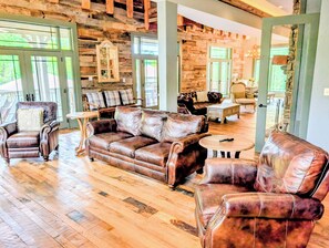 A spacious living room with leather sofas, wooden flooring, and large windows allowing natural light.