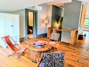 A room with a wooden floor, a round wooden table, two chairs, a white cabinet, and a doorway leading to another room.