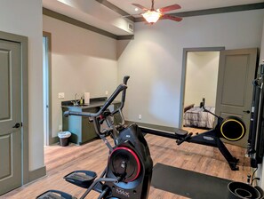 A home gym with an elliptical trainer, a stationary bike, and a ceiling fan.