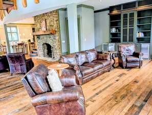 A spacious living area with leather sofas, a stone fireplace, and a bookshelf.